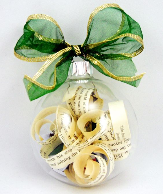 Image of a clear ornament with book page strips inside topped with a green bow.