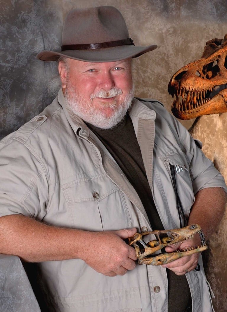 Image of a man wearing a hat holding a dinosaur skull.