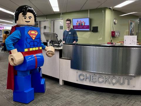 Image of LEGO Superman standing in front of the checkout desk at the library